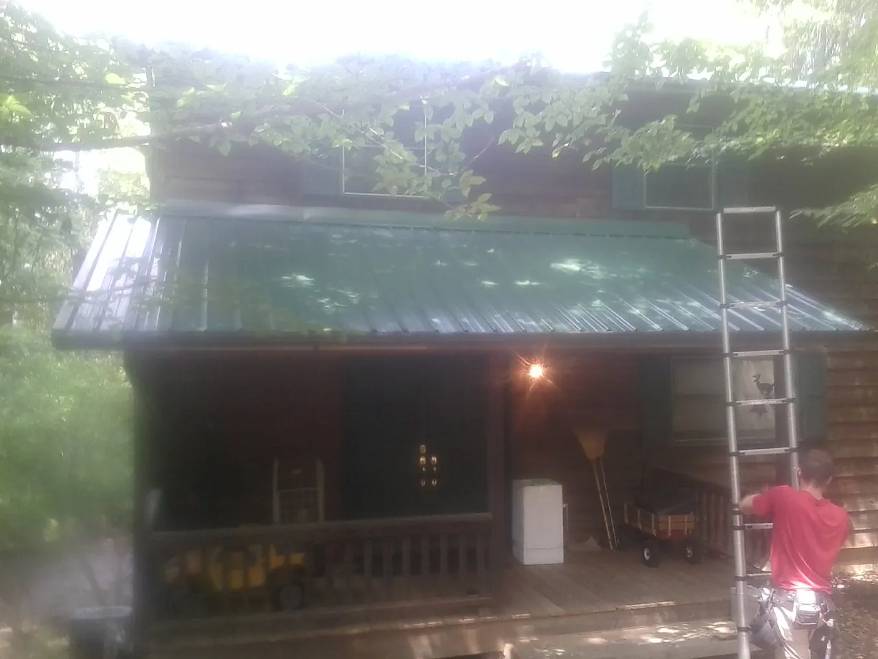 Worker on a ladder at the green porch roof of a wooded cabin in Pierce